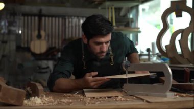 Yetenekli bir Luthier atölyesinde bir akustik gitarın vücudunu zımparalamak için çok çalışıyor. Detaylara dikkat etmek Luthier 'in elleri ve gitarının yakın görüntüsünde açıkça görülüyor..
