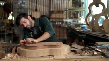 Yetenekli bir Luthier atölyesinde bir akustik gitarın vücudunu zımparalamak için çok çalışıyor. Detaylara dikkat etmek Luthier 'in elleri ve gitarının yakın görüntüsünde açıkça görülüyor..