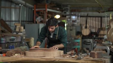 Yetenekli bir Luthier atölyesinde bir akustik gitarın vücudunu zımparalamak için çok çalışıyor. Detaylara dikkat etmek Luthier 'in elleri ve gitarının yakın görüntüsünde açıkça görülüyor..