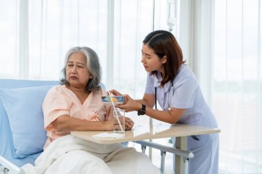 Tedavi sırasında hastaneye yatırılan yaşlı Asyalı hasta hemşire bir hastaya bakıyor ve onu besliyor ama iştahsızlığı var. Hemşire, hastane ya da klinikte hastalara bakar..