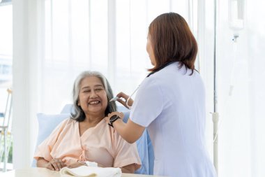 Yaşlı Asyalı hasta hastaneye yattı hemşire moral konuşması yaptı ve hastanın saçını taradı. Hemşire, hastane ya da klinikte hastalara bakar..