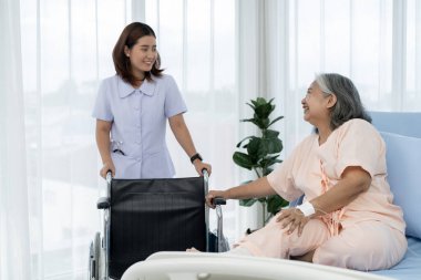 Bir hemşire, yaralı bacağının röntgenini çekmek için yaşlı bir Asyalı hastayı almak için tekerlekli sandalye getiriyor. Hemşire, hastane ya da klinikte hastalara bakar..