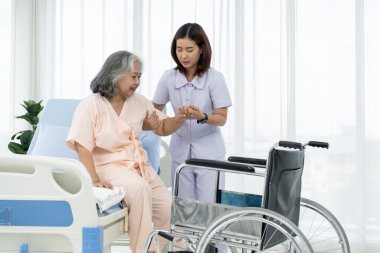 Bir hemşire, yaşlı bir Asyalı hastayı bir kazada bacağının röntgenini çektirmek için tekerlekli sandalyeye taşıyor. Hemşire, hastane ya da klinikte hastalara bakar..