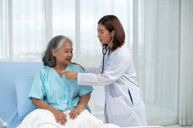 Yaşlı bir Asyalı kadın hasta göğüs hastalığından hastaneye kaldırıldı. Kadın doktor akciğer solunumunu kontrol etmek için stetoskop kullanıyor. Tıbbi ve sağlık hizmetleri kavramı