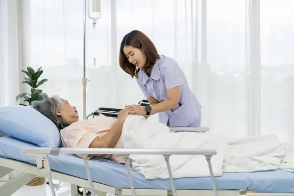 Elderly Asian patient admitted to hospital A nurse or caregiver of an elderly patient is helping to cover blanket a patient lying in bed. Nurses care for patients in hospitals or clinics.