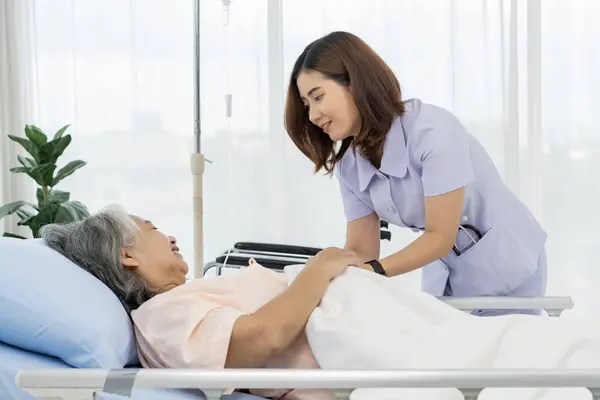 Elderly Asian patient admitted to hospital A nurse or caregiver of an elderly patient is helping to cover blanket a patient lying in bed. Nurses care for patients in hospitals or clinics.