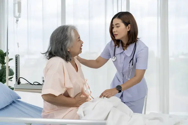 Asian elderly patient with stomachache. A nurse or caregiver for an elderly patient is helping a patient with severe stomach problems. Nurses care for patients in hospitals or clinics.