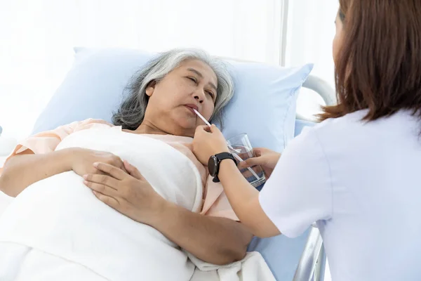 Elderly Asian patient admitted to hospital She had symptoms of fatigue, thirst and fever. The nurse put water in a glass and fed it to her through a straw. Nurses care for patients in hospitals