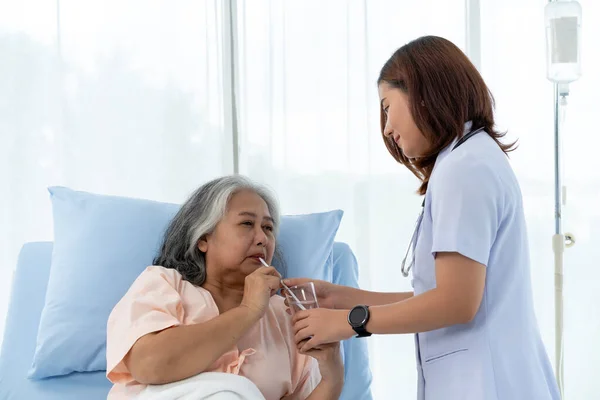 Elderly Asian patient admitted to hospital During her recovery, the nurse took care of her and gave her water when she was thirsty. Nurses care for patients in hospitals or clinics.