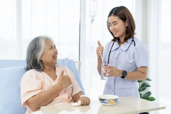 Elderly Asian patient admitted to hospital The nurse gave her encouragement and gave her a thumbs up for taking care of herself until she was nearly fully recovered. A nurse takes care of patients