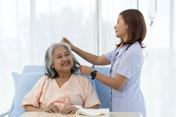 Elderly Asian patient admitted to hospital The nurse gives a pep talk and combs the patient\'s hair. A nurse takes care of patients in a hospital or clinic.