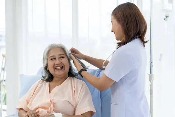 Elderly Asian patient admitted to hospital The nurse gives a pep talk and combs the patient\'s hair. A nurse takes care of patients in a hospital or clinic.
