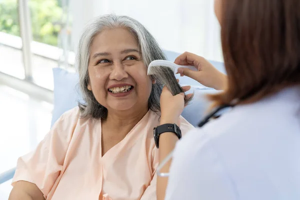 Close-up photo of an elderly Asian patient admitted to the hospital. The nurse gives a pep talk and combs the patient\'s hair. A nurse takes care of patients in a hospital or clinic.