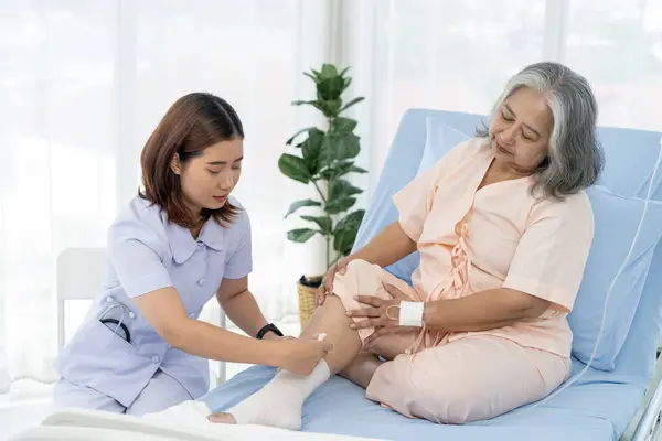 Elderly Asian patient admitted to hospital A nurse cares for a patient\'s injured leg bandage. A nurse takes care of patients in a hospital or clinic.