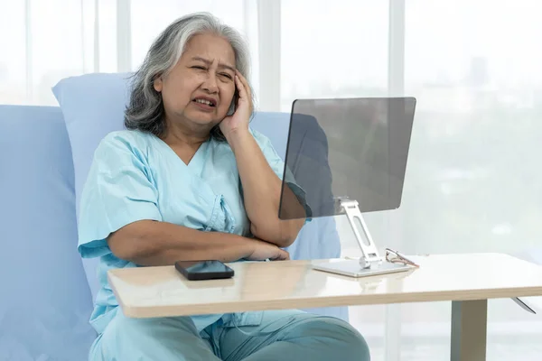 Elderly Asian patient admitted to hospital. Mock up the screen for additional information later. Patients use video conference to talk to doctors via computer. Telemedicine concept