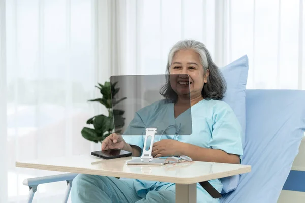 Elderly Asian patient admitted to hospital. Mock up the screen for additional information later. Patients use video conference to talk to doctors via computer. Telemedicine concept