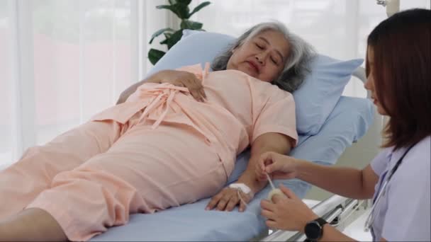 手持特写镜头 一位女护士为一位年迈的亚洲女性病人插入了一条四线 她用胶带把绳子固定住 护士在医院照顾病人 — 图库视频影像