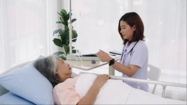 El kamerasıyla çekilen yaşlı Asyalı hasta öksürük ve ateşi olduğu için hastaneye yatırıldı. Hemşire ateşini ölçmek için dijital termometre kullanıyor. Hastanelerde ya da kliniklerde hastalara hemşireler bakar.