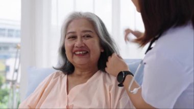 Yakın çekim, hastaneye yatırılan yaşlı Asya 'lı hasta hemşire moral konuşması yapıyor ve hastanın saçını tarıyor. Hemşire, hastane ya da klinikte hastalara bakar..