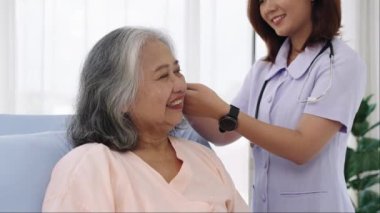Yakın çekim, hastaneye yatırılan yaşlı Asya 'lı hasta hemşire moral konuşması yapıyor ve hastanın saçını tarıyor. Hemşire, hastane ya da klinikte hastalara bakar..