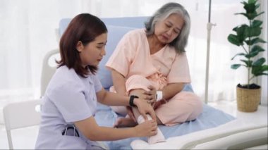 Elle yapılan iğne, yaşlı Asyalı bir hasta hastaneye yatırıldı. Bir hemşire yaralı bir hastanın bacağındaki bandajla ilgileniyor. Hemşire, hastane ya da klinikte hastalara bakar..