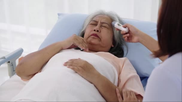 ハンドヘルドショット 高齢のアジアの患者は 彼女が咳と発熱を持っていることを入院しました 看護師は温度を取るためにデジタル温度計を使用しています 病院やクリニックの患者さんのケア — ストック動画