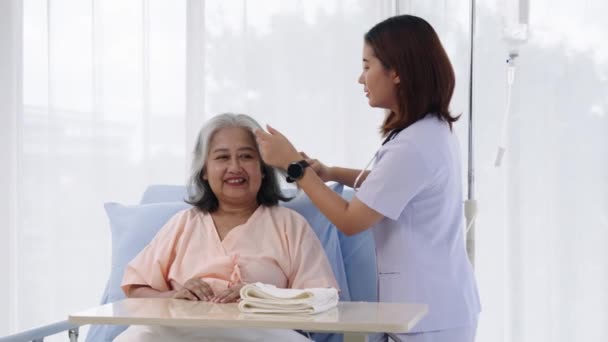 ハンドヘルドショット 病院に入院した高齢アジアの患者 看護師はペプトークをし 患者の髪を組み合わせます 看護師が病院やクリニックで患者の世話をします — ストック動画