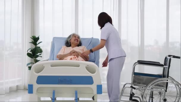 一名护士将一名亚洲老年病人从轮椅上抬到床上 在此之前 他带着他对车祸中受伤的腿进行了X光检查 护士在医院照顾病人 — 图库视频影像