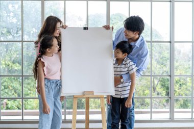 Mutlu Asyalı aile çocuklarının boyama sayfalarını gösteriyor ve gurur duyuyorlar. Anne ve baba çocuklarına hobisinde destek oluyor. Aile mutluluğu oturma odasında.