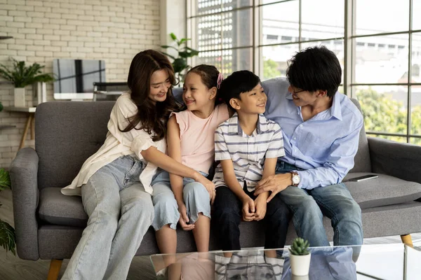 Happy family talking at home in the living room. A young man and woman sit on the sofa with their son and daughter, happily spending time together and chatting about various matters.