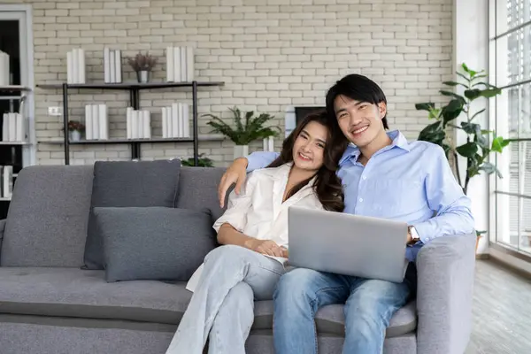 Happy family in the living room. Young couple planning future together on couch with Laptop internet, Parents sit on sofa resting using pc online services plan family life