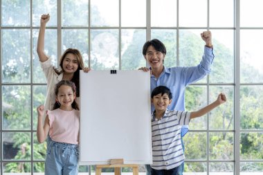 Mutlu Asyalı aile çocuklarının boyama sayfalarını gösteriyor ve gurur duyuyorlar. Anne ve baba çocuklarına hobisinde destek oluyor. Aile mutluluğu oturma odasında.