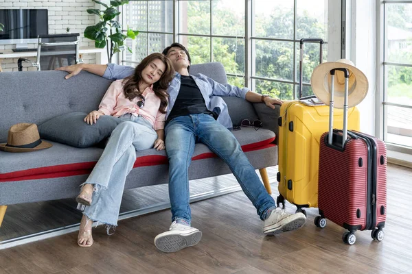 Tired couple returning home from a summer vacation trip Sitting asleep on the sofa in the living room with a yellow and red suitcase. Returning from adventure and vacation in holiday.