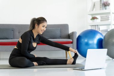 Bir kadın dizüstü bilgisayarının önünde yoga minderinin üzerine uzanır. Çevrimiçi fitness ve sağlıklı yaşam tarzının faydalarından zevk alır..