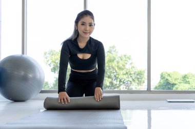 Oturma odasında yoga minderini katlayan bir kadın. Bu fotoğraf, yoga yaşam tarzının popülaritesini yakaladığı için mikrostok web siteleri ve diğer çevrimiçi platformlar için mükemmel..