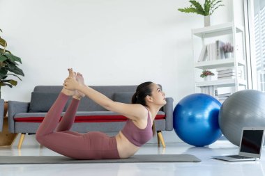 Spor giyimli Asyalı genç bir kadın evde paspasın üzerinde yoga yapıyor, nefesine odaklanıyor ve kaslarını geriyor. Yoga esnekliği, gücü ve dengeyi geliştirmek için harika bir yoldur..