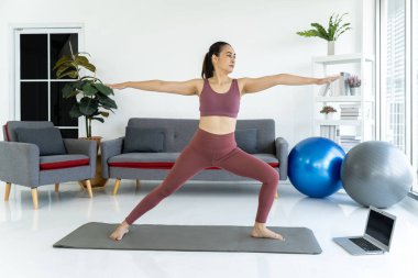 Warrior Poose 'daki zarif Asyalı kadın huzurlu oturma odasında yoga minderinde dengesini buluyor..
