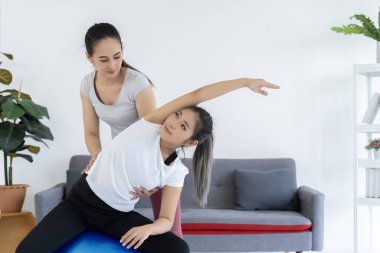 Kişisel antrenör, spor salonunda bir fitness topunu esneten bir müşteriye yardım ediyor. Bu görüntü, kişisel spor ayakkabıları ve spor salonları için pazarlama malzemeleri için mükemmel..