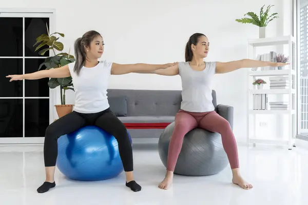 Two women sitting on exercise balls in living room, working out and enjoying a healthy lifestyle. This image  for fitness, health, and lifestyle bloggers, as well as for businesses promoting fitness