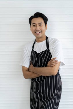 Genç ve yakışıklı bir barista gülümsüyor ve beyaz tişört ve önlük giyerek tezgah kuruyor. Moda ve şık bir kafede çalışıyor. Lezzetli kahve servisi yapıyor..
