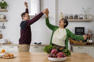 Neşeli Olgun bir çiftin portresi mutfakta dans ederken eğleniyor ellerinde portakal suyu, gülümsüyor ve birlikte mutlu bir şekilde gülüyorlar..