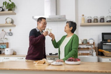 Neşeli, olgun bir çift mutfakta birlikte vakit geçirir, gülümser ve ellerinde şarap kadehleriyle eğlenir ve dans ederler.