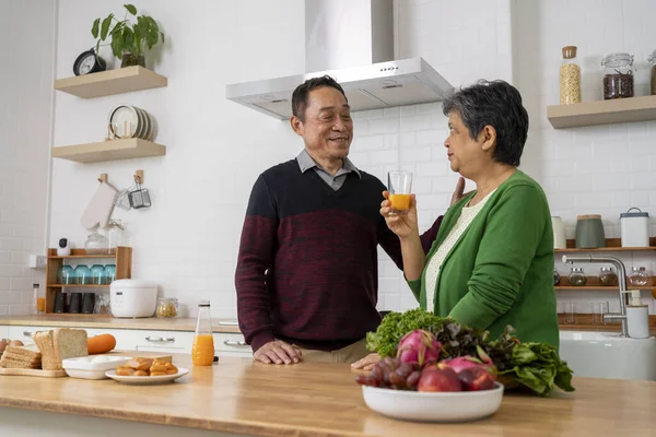 Portrait of Happily Mature couple have spending time together in kitchen, Cute husband smile and pouring orange juice to serve his wife during cooking meal at home