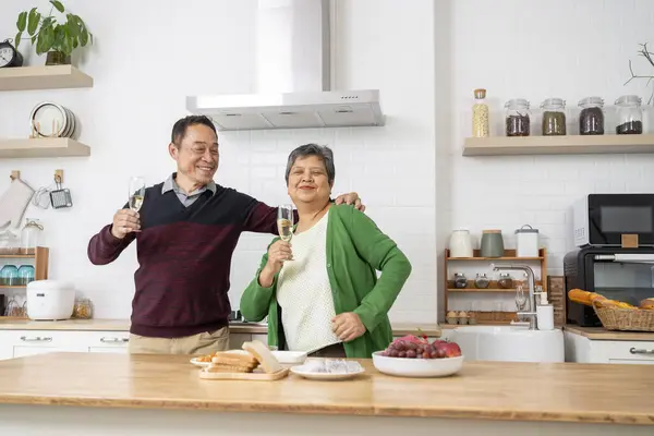Cheerful Mature couple have spending time together in kitchen, They are smile and holding glass of wine clinking and dance with fun and happiness