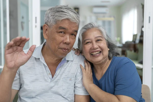 Portrait of cheerful husband and wife smiling and looking at camera, Asian mature couple embracing with love and happy together at home