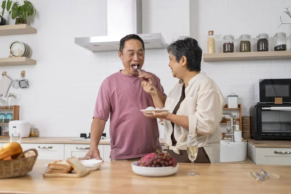 Asian mature couple eating dragon fruit in kitchen, Wife feeding tasting fresh fruit to husband, They are talking and smile with happiness together