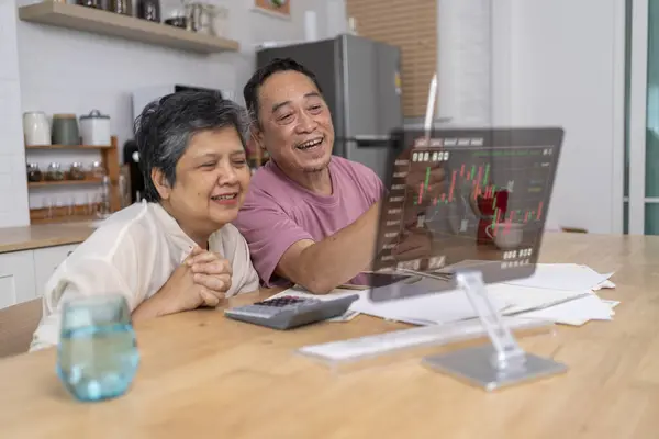 Portrait of Senior asian couple learning about new technology Modern life after retirement at home excited with graph of stocks rising on screen, the transparent monitor with graphic about financial