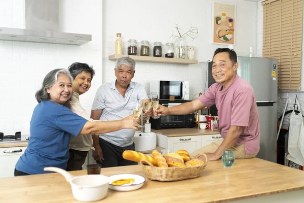 Group of Happy Asian senior drinking wine to celebrate and talking with fun, cheering glass of wine and drink while dining at home together, looking at camera and smiling
