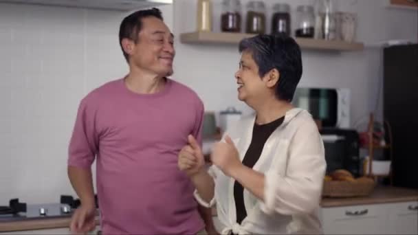 ハンドヘルドミディアムショット 陽気な夫と妻は微笑み キッチンで踊ることを楽しんで アジアの成熟したカップルダンスと一緒に家で幸せに笑います — ストック動画