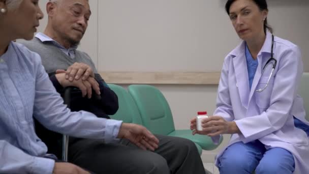 手持缩放镜头 年轻的女性理疗师检查坐在那边的成年男性病人和他的妻子的膝盖 他们正在医院里一起讨论医学问题 — 图库视频影像